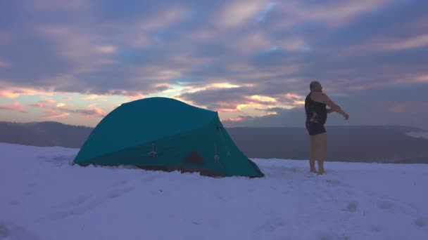 穿着短裤的徒步旅行者从帐篷里出来 在寒冷的天气里 日落的时候 在寒冷的冬山里 — 图库视频影像