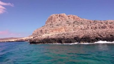 Dalgaların kayalıklara çarptığı engebeli güzel sahil şeridi, hareket eden teknenin manzarası.