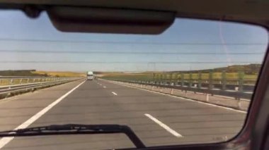 Otoyolda araba sürüyor, tepelerden geçiyor, bir yaz gününde. Arabanın arka tarafında.