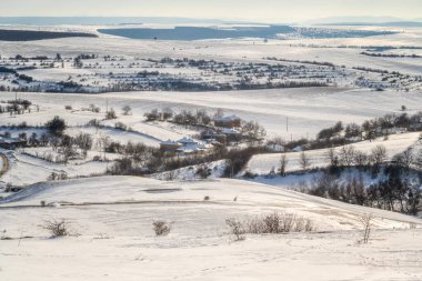 Karla kaplı tepelerin arasına kurulmuş küçük bir köyle harika bir kış manzarası.