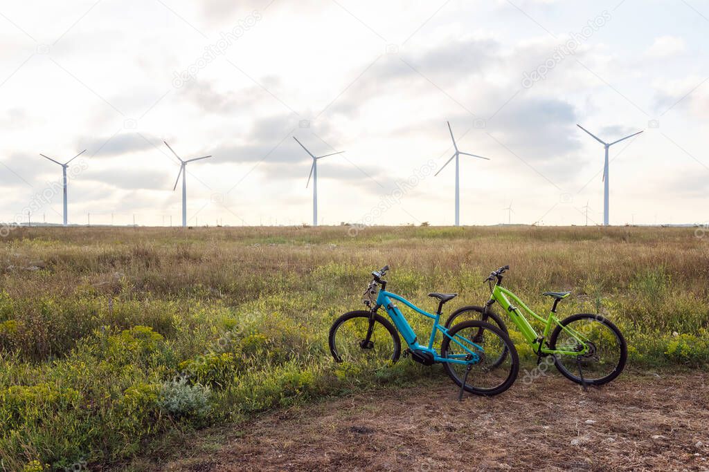 Amazing view with electric bikes in a field against the backdrop of wind turbines. Green energy, sustainable alternative electricity, no pollution environment.