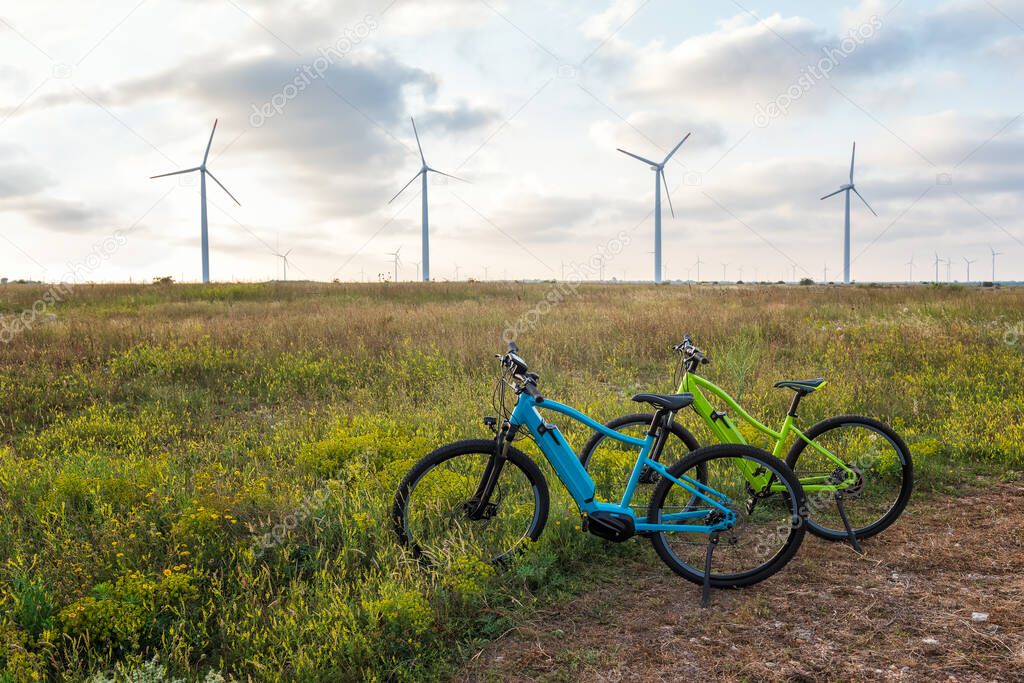 Amazing view with electric bikes in a field against the backdrop of wind turbines. Green energy, sustainable alternative electricity, no pollution environment.