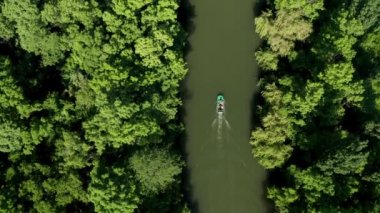 Kalın yeşil bir ormanın içinden geçen bir nehirde, motorlu bir teknenin üzerinden insansız hava aracı uçuşu.