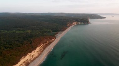 Sonsuz kumlu plajlı ve sabahları aşırı gelişmiş tepeleri olan kayalık bir sahil şeridinin üzerinde insansız hava aracı uçuşu.