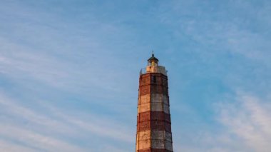 Mavi sabah gökyüzünün arka planında eski bir deniz fenerinin hızlandırılmış videosu. Görüntüyü kapat.