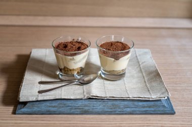 Küçük cam kaselerde tiramisu kremi ve yumuşak odaklı iki kaşık.