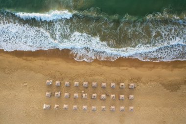 Pahalı deniz dalgaları, Karadeniz kıyısı, Bulgaristan yakınlarındaki saman güneşlikleri ve güneşlikleriyle boş ve güzel kumlu bir plajın üzerindeki hava manzarası