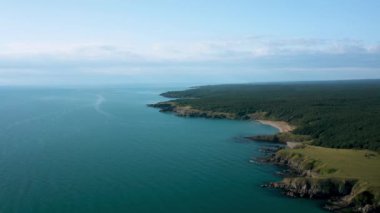 Vahşi plajları, yeşil ormanları ve turkuaz deniz suları olan kayalık bir sahil şeridinin üzerinde insansız hava aracı uçuşu. Üst görünüm.