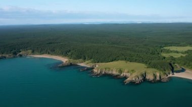 Vahşi plajları, yeşil ormanları ve turkuaz deniz suları olan kayalık bir sahil şeridinin üzerinde insansız hava aracı uçuşu. Üst görünüm.