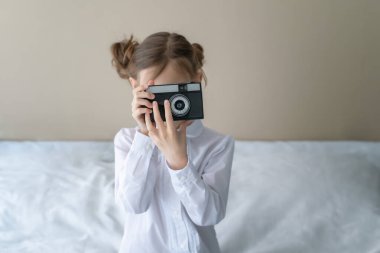 Güzel beyaz bir kızın portresi, şık bir saç stili, kot pantolon giyiyor ve elinde klasik bir fotoğraf makinesi tutan beyaz bir gömlek.