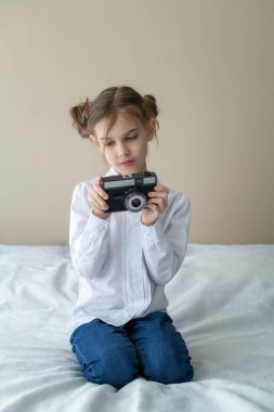 Güzel beyaz bir kızın portresi, şık bir saç stili, kot pantolon giyiyor ve elinde klasik bir fotoğraf makinesi tutan beyaz bir gömlek.