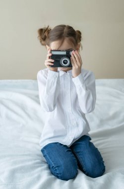 Güzel beyaz bir kızın portresi, şık bir saç stili, kot pantolon giyiyor ve elinde klasik bir fotoğraf makinesi tutan beyaz bir gömlek.