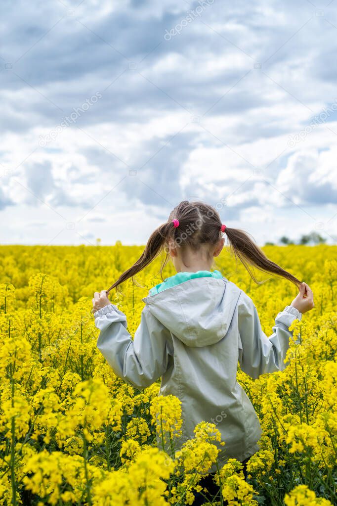 Close up rear view of a beautiful girl in a rapeseed field. A child in a blooming field with yellow flowers. 