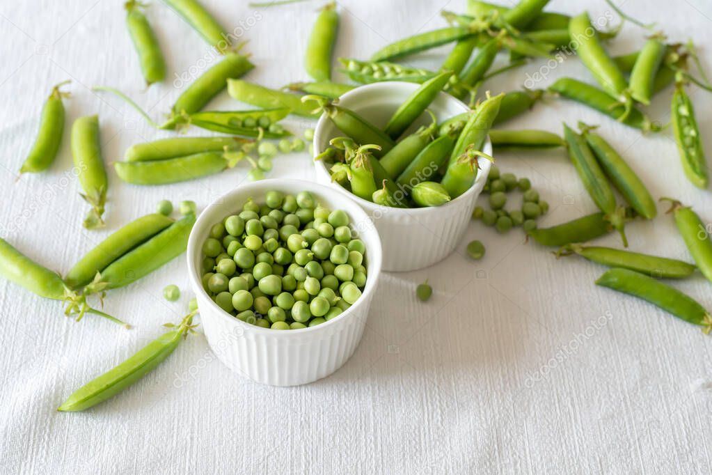 Fresh green peas decoration on a white textile background, top view