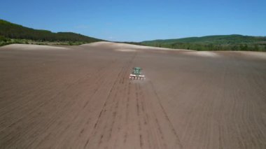 Resmedilmeye değer tepeleri olan güzel bir tarlanın havadan görünüşü ve pullukla hareket eden bir traktör, tozu kaldırıyor, tarlayı ekime hazırlıyor.