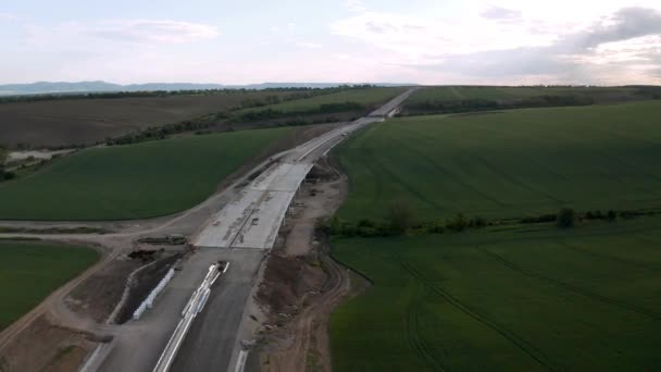 緑の圧延場とそれらを通過する新しく建設された高速道路で美しい自然の上にドローン飛行 — ストック動画