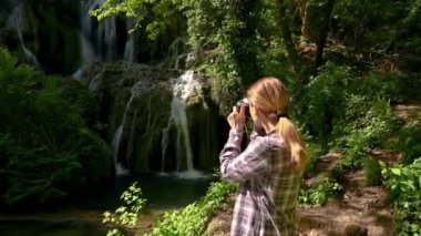 Bir kadının resim çektiği ve yeşil bahar ormanlarında güzel bir şelalenin keyfini çıkardığı video, Kruşuna Şelalesi, Balkan Dağları, Bulgaristan.