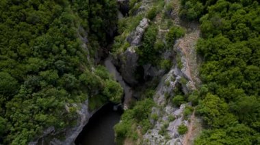 Resimli bir nehir kanyonu üzerinde insansız hava aracı uçuşu. Yüksek sarp kayalıklar yeşilliklerle kaplanmış.