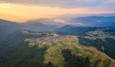 Resmedilmeye değer yeşil dağ yamaçlarının ve gün batımının altın saatinde içine yerleştirilmiş küçük bir köyün havadan görünüşü, Bulgaristan 'daki Rhodopi Dağları