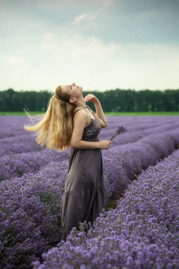 Portrait of a woman in a dress, enjoying the sense of blooming lavender field at golden hour before sunset