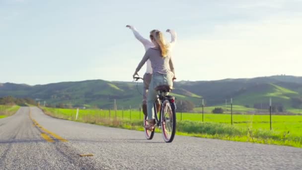 Två Glada Tjejer Rider Cykel Med Händer Luft Solnedgången — Stockvideo