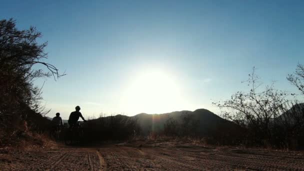 Silhouette två människor mountainbike vid solnedgången utanför — Stockvideo