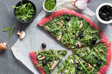 Vejetaryen kırmızı pizza. Ispanak soslu pancar pizzası, vegan peyniri, mantar, zeytin ve soğanla süslenmiş taze roka. Sağlıklı ev yapımı fast food pizza, koyu bir arka plan, üst manzara, parçalar..
