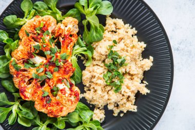 Kavrulmuş karnabahar bifteği, Qinoa, kuzu marulu ve nar ile servis edilir. Sağlıklı beslenme, bitki temelli et ikame konsepti.