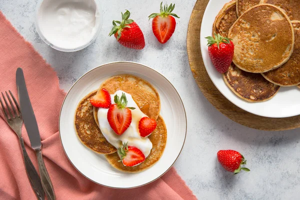A plate of vegan pancakes with fresh strawberries and cream on a white background.