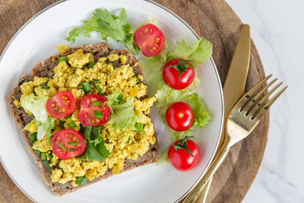 Tofu scramble with tomatoes and greens on toast on a  plate. Healthy vegan food concept.