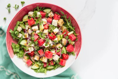 Taze yaz karpuz salatası tofu, roka, salatalık, kırmızı soğan, kuzu marulu çiçekler ve açık mermer zemin üzerinde vinaigrette sosu. Sağlıklı vejetaryen yemekleri.