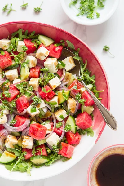 Taze yaz karpuz salatası tofu, roka, salatalık, kırmızı soğan, kuzu marulu çiçekler ve açık mermer zemin üzerinde vinaigrette sosu. Sağlıklı vejetaryen yemekleri.