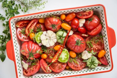 Domates, sarımsak ve otlar seramik tabakta, pişirmeye hazır..