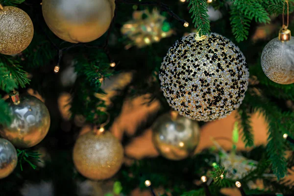 Boule de Noël avec des pierres de verre noires et des boules floues dorées sur une branche verte avec une guirlande jaune. Fond sombre flou — Photo