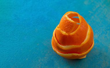 Meyveli sanatçı imajı. Arka planda mavi ahşap bir masa üzerinde spiral mandalina kabuğu var. Portakal kabuğuyla yakın çekim ve doku.