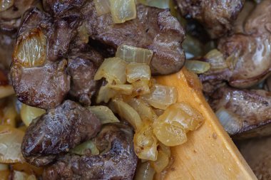 Kızarmış tavuk ciğeri ve sarımsak, tavada soğan ve tahta kaşık. Yemek pişti. Yüzeyin derinliği. Üst görünüm.