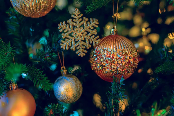 Bola de vidro festivo de ouro com brilhos coloridos, floco de neve na árvore de Natal e belo bokeh amarelo de guirlanda brilhante. — Fotografia de Stock