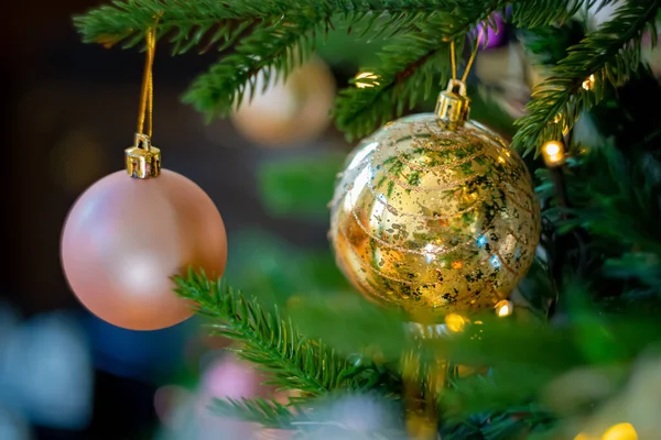 Gold- und rosafarbene Festtagskugeln am Weihnachtsbaum und ein wunderschönes gelbes Bokeh aus leuchtenden Girlanden. Kopierraum. — Stockfoto