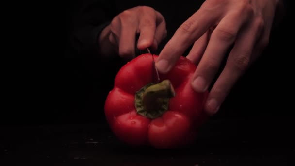 Mens händer skära röd paprika i 2 delar på en mörk bakgrund — Stockvideo