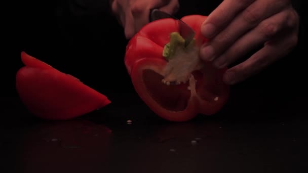 Mens händer skära röd paprika i flera delar på en mörk bakgrund — Stockvideo
