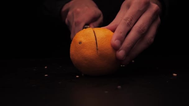 Herrenhände schneiden eine gelbe, orangefarbene Frucht auf dunklem Hintergrund in zwei Teile — Stockvideo