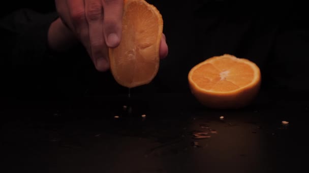 Las manos masculinas exprimen el jugo de media naranja amarilla sobre el fondo oscuro — Vídeos de Stock