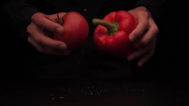 Le mani di un uomo raccolgono un peperone rosso e un pomodoro su uno sfondo scuro dal tavolo — Video Stock