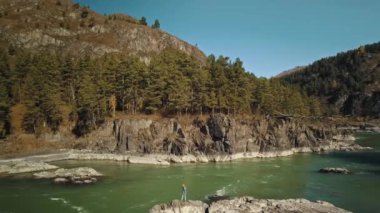 Dağ manzaralı yeşil nehir Katun. Kayaların üzerinde yürüyen genç bir kız. Ormanlı güzel bir sonbahar dağı vadisi. Chemal Köyü, Altai Cumhuriyeti, Rusya