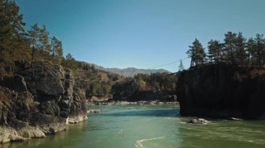 Dağ manzaralı yeşil nehir Katun. Kamera iki ada arasındaki bir köprünün altında uçuyor. Chemal Köyü, Altai Cumhuriyeti, Rusya
