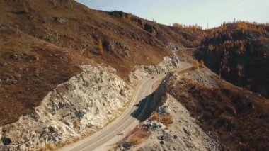 Yüksek irtifada Serpentine dağ yolunun havadan görüntüsü. Güzel sonbahar altın vahşi manzarası: dolambaçlı zorlu yol, orman, sarı ve kırmızı yapraklı ağaçlar, büyük dağlar, sarp kayalıklar