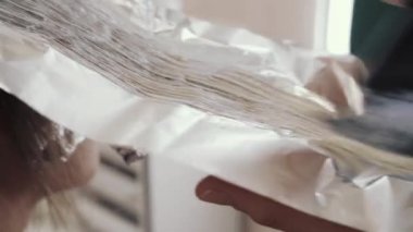 Bir kızın uzun kahverengi saçlarını ön plana çıkarma sürecine yakın plan. Kuaför, kızın güçlü ve güzel saçlarını boyamak, saçlarını taramak, ıslak saçlarını folyoya sarmak için hazırlar.