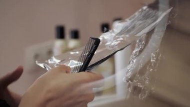 Bir kızın uzun kahverengi saçlarını ön plana çıkarma sürecine yakın plan. Kuaför, kızın güçlü ve güzel saçlarını boyamak, saçlarını taramak, ıslak saçlarını folyoya sarmak için hazırlar.