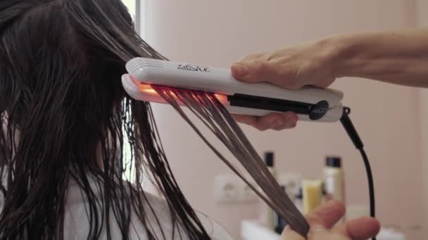 Gros plan sur le processus de diagnostic et de traitement d'une fille cheveux longs bruns pour la santé des cheveux. Un coiffeur goutte une solution de restauration spéciale sur cheveux mouillés dans un salon de beauté spécial — Video