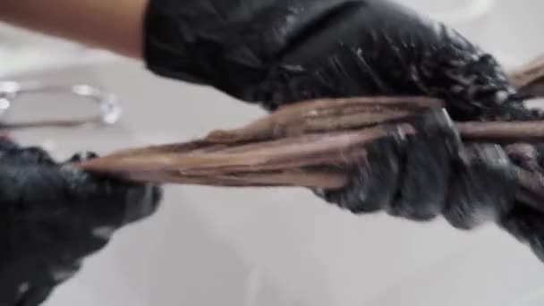 Detailní záběr procesu zvýrazňování a mytí dívek dlouhé hnědé vlasy pro zdraví vlasů. Kadeřník v rukavicích připravuje silné krásné vlasy dívky pro zvýraznění, mytí a — Stock video